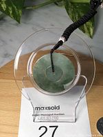 Inset circular green Burma jade pendant on clear display stand with black braided adjustable rope attached.