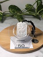 Front view of white rectangular Burma jade pendant with carved dragon design on black adjustable rope necklace next to a coin for scale