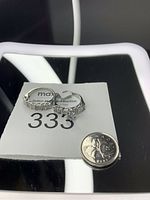 Two silver or white gold rings with stones, size 10, shown with a Canadian quarter for scale on a reflective surface.
