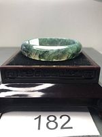 Moss agate bangle bracelet displayed on decorative black wooden stand, showing translucent green stone with mossy inclusions.
