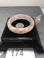 Round red hematoid quartz bangle bracelet with visible internal hematite inclusions placed on black display stand next to US quarter for scale.