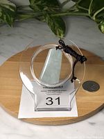 Front view of square Burma jade pendant on adjustable black rope, placed on a clear display stand with a quarter for size reference.
