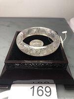Front angled view of the Super 7 quartz bangle showing translucence and black inclusions with a coin for scale.