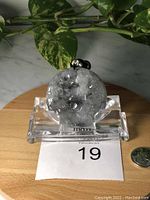 Front view of round translucent jade pendant with dark mountain-like inclusions, displayed on clear stand with auction label and quarter coin for scale.