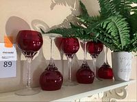 Red stemware glasses and a red glass mug with clear textured stems and bases, displayed with decorative plant and white ceramic floral embossed mug.