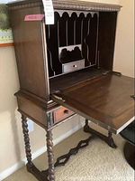 Side angle displaying fold-down writing surface opened, barley twist legs, and trestle foot base