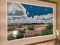 Framed landscape art print showing clouds, rocks, and green bushes.