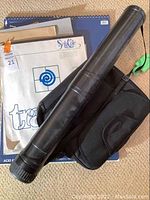 Photo showing art pads stacked on the floor including tracing pad, newsprint, and large drawing pads with a black canvas storage tube and a black carrying bag placed on top.