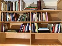 Wide shot of wooden bookshelf with several shelves filled to half or more with books of various sizes and colors