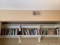 Wide angle view showing multiple assorted books organized on a white wall shelf.