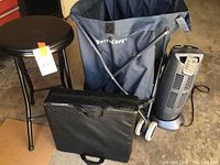 Folding rolling canvas cart with blue canvas bag next to black round stool and portable folding seat on floor
