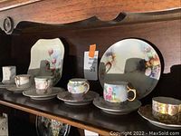 Overview of five decorative china teacups on their matching saucers lined up on wooden shelf featuring floral and gold trim designs.