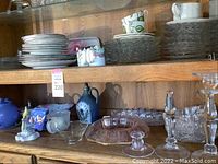 Wide view of shelf showing blue teapot, plates, coasters, and various glassware items