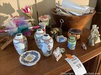 Overview of ceramic floral vases, large wooden salad bowl, false flowers, and small trinkets displayed on wooden surface.