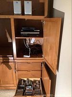 Image showing wooden cabinet housing two white Aiwa compact speakers on top shelves and a lower shelf with multiple music CDs in jewel cases arranged.