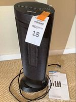 Black Honeywell tower fan approximately 2 feet tall with visible power cord and user manual on floor nearby
