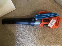 Black & Decker plug-in electric leaf blower with visible black nozzle, orange motor body, and blue power cord coiled on top.