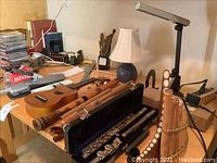 Wide view of table with ukulele, wooden recorders, bamboo panpipes, flute in case, lamps and assorted office supplies.