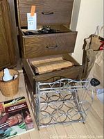 Four bamboo placemats rolled inside a wooden drawer, metal wine rack holding twelve bottles placed in front, 'The Microwave Guide & Cookbook' on the floor next to the rack.