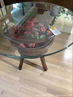 Angle view showing the dark rattan base with curved legs and the clear round glass tabletop with floral decoration underneath.