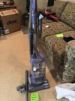 Full view of Shark Navigator Lift-Away upright vacuum showing handle, dust cup, and base with brush head, placed on carpet next to couch.