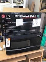 Sharp Carousel microwave oven with black body and keypad. LG microwave oven box placed on top, showing brand, features and specifications.