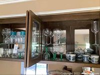 Glass stemware on upper shelf including clear wine glasses, green-stemmed cocktail glasses, and a set of ceramic tea items with blue and white scenic designs on lower shelf.