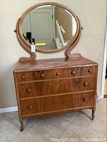 Front view of wooden antique dresser with attached oval mirror showing four drawers and wooden knobs.
