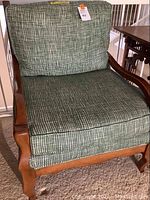 Full view of wooden armchair with green and white checked cushions showing carved leg and armrest details.