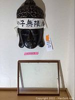 Front view of dark hand-carved wooden Japanese mask with white headband and Japanese characters.