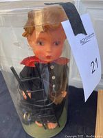 Front view of the Goebel doll inside the original plastic cylinder container, showing the doll's face, hair, and upper torso.