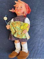 Front view of the Goebel doll showing full traditional outfit, including the red headscarf, brown dress, yellow apron with attached chick, white socks, and brown shoes.