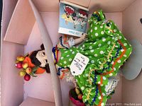 Top-down view of Madame Alexander Brazil doll in original pink box with a booklet and wear on the box.