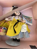Front view of Madame Alexander doll in original box with yellow dress and basket of hats.