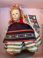 Front view of the Madame Alexander doll in traditional Polish outfit inside the original box showing intricate embroidered details and headband with flowers.