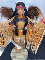 Front view of the Mahala Native American doll showing full body, fringed dress, beadwork, feather wings, and wooden base with nameplate.
