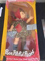 Full view of Poor Pitiful Pearl doll inside original yellow and pink box with visible wear and tape repairs.