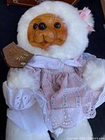Front view of Sally Bear with detailed wooden face, dressed in pink floral dress with white lace and faux fur hood, with original tag visible.