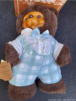 Front view of Timmy Bear showing carved wooden face, brown fur body, blue and white checkered overalls and original box behind