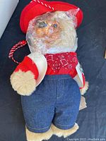 Fox plush stuffed animal with red hat, bandana, denim pants, partially covered in plastic wrap