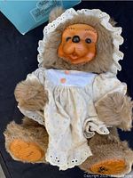 Full view of Raikes Bear Jenny doll showing plush fur body, wood face, and lace-trimmed bonnet and outfit.