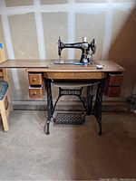 Full view of the antique Singer sewing machine mounted on oak cabinet with treadle base, showing top working surface and side drawers.
