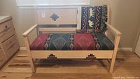 Front view of wooden bench with Santa Fe style geometric patterns on back and front panels with padded Southwestern style fabric seat cushion and matching throw pillow.