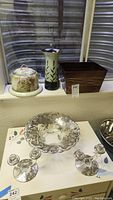 Photo showing cheese plate with cream to green gradient and grapevine design, tall ceramic vase with leaf motif, and wooden container