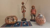Wide shot showing all items: two conquistador figurines, two decorative gourds, and a small rug with llama patterns.