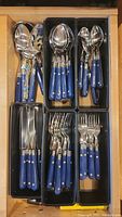 Drawer-organized flatware with blue handles divided into separate compartments by type (forks, spoons, knives, serving pieces)