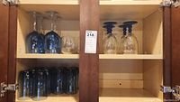Top shelf of cabinet holding blue glass wine glasses, clear wine glasses with blue stems, and other stemware.
