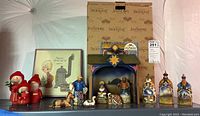 Wide view of all figurines and framed art on shelf with Jim Shore branded boxes behind the nativity set.