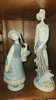 Two figurines displayed side by side on wooden shelf