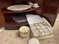 China cups and saucers stacked in storage container, ceramic turkey platter and more china cups on shelf within cabinet.
